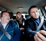 Imagen de un examen de conducir. Un examinador, en el asiento trasero, indica a un alumno el destino al que debe dirigirse